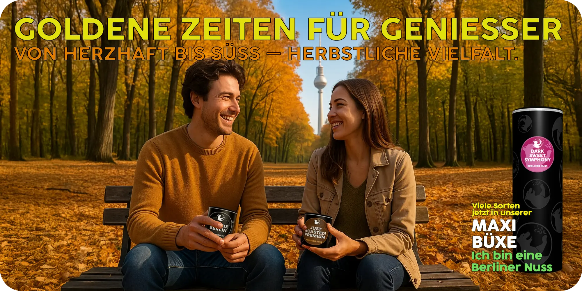 Ein junger Mann und eine junge Frau sitzen auf einer Parkbank im Herbst und halten je eine Dose Nüsse in der Hand. Im Hintergrund sieht man den Fernsehturm.